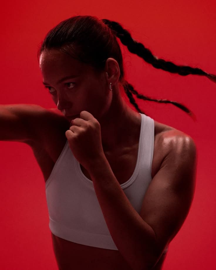 Een jonge vrouw in een witte sporttop staat in dekking voor een rode achtergrond