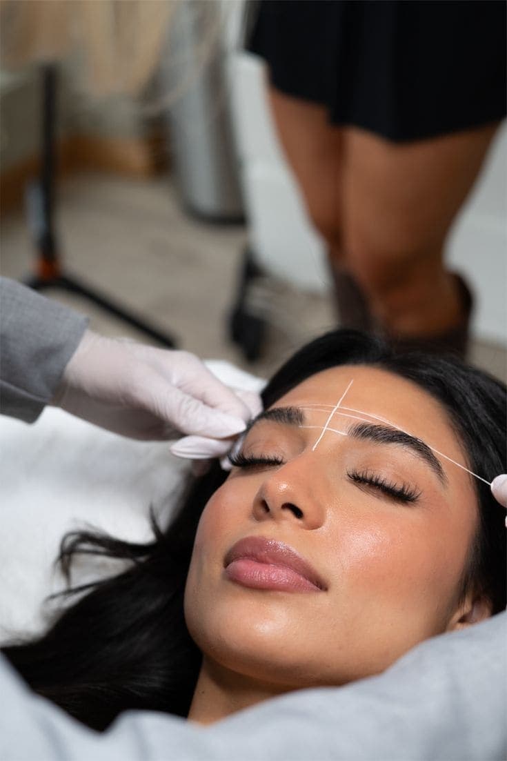 Een klant met gesloten ogen krijgt threading aan haar wenkbrauwen