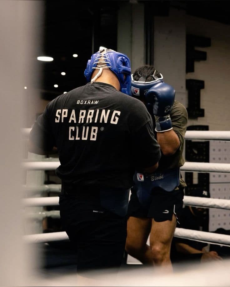 Two fighters in blue headguards sparring in the ring of a martial arts school