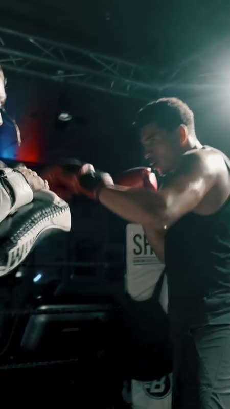 Een trainer houdt de stootkussens vast voor een lid dat bokst