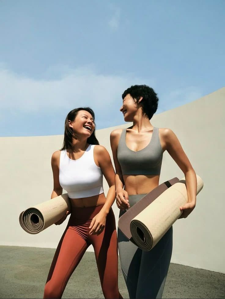 Twee vrouwen lachen buiten met een opgerolde mat onder de arm