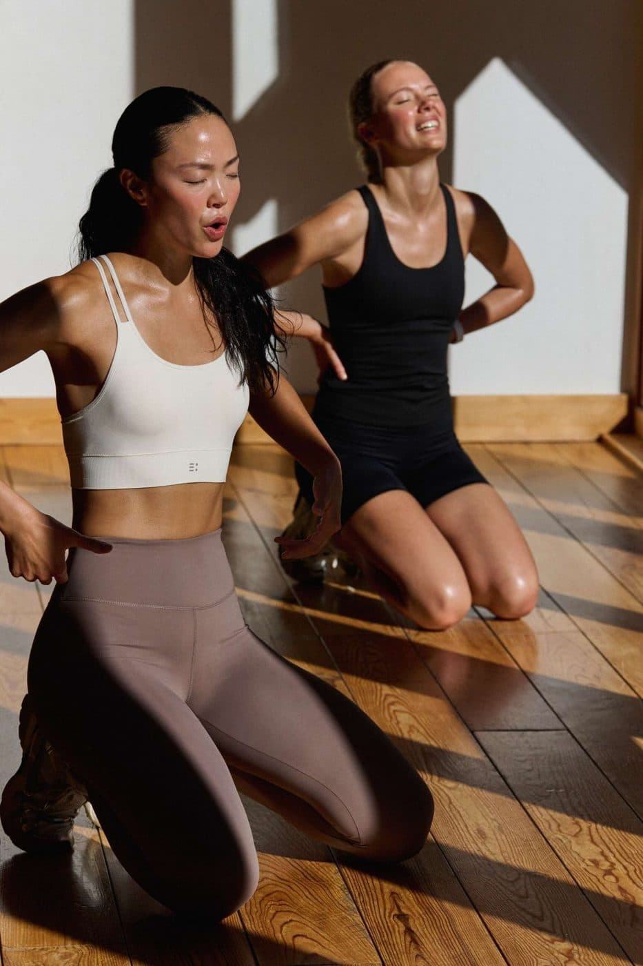 Twee vrouwen knielen op een houten vloer in een studio